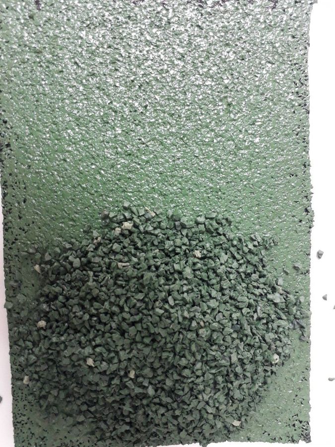 Granulado de caucho verde ligado formando una superficie continua, con granulado suelto sobre ella