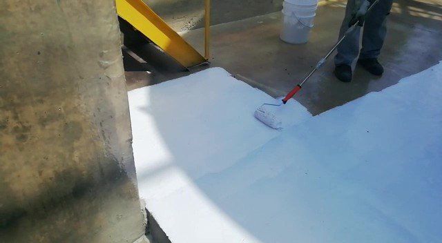 Aplicación de pintura de poliuretano blanca con rodillo sobre piso de hormigón